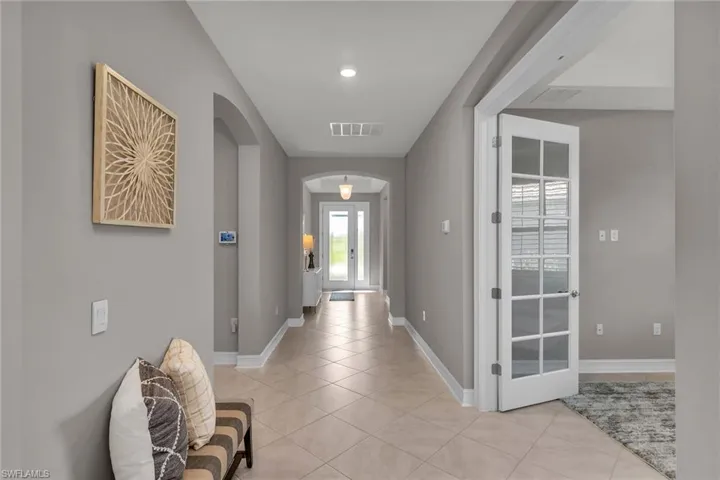 Entryway with arched walkways, light tile patterned flooring, visible vents, and baseboards