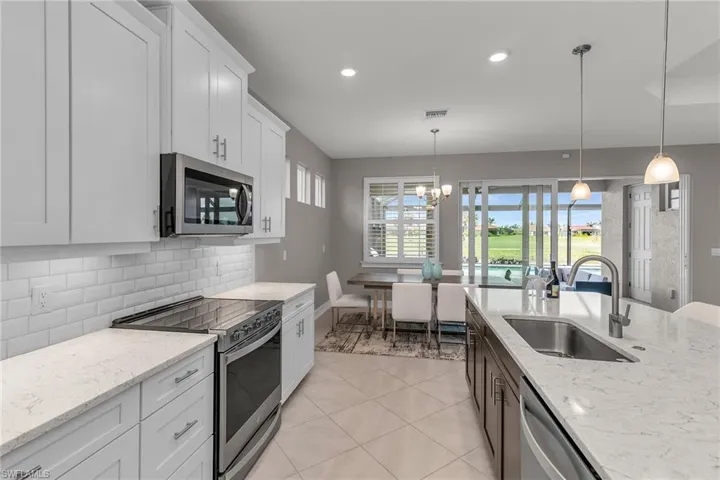 Kitchen with decorative backsplash, appliances with stainless steel finishes, white cabinets, light tile patterned flooring, and a sink