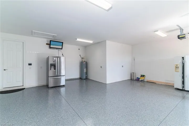 Garage with stainless steel fridge, white fridge with ice dispenser, a garage door opener, and electric water heater