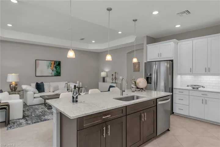 Kitchen featuring stainless steel appliances, a raised ceiling, visible vents, a sink, and an island with sink