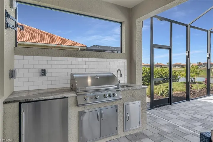 View of patio featuring a sink, glass enclosure, an outdoor kitchen, and a grill