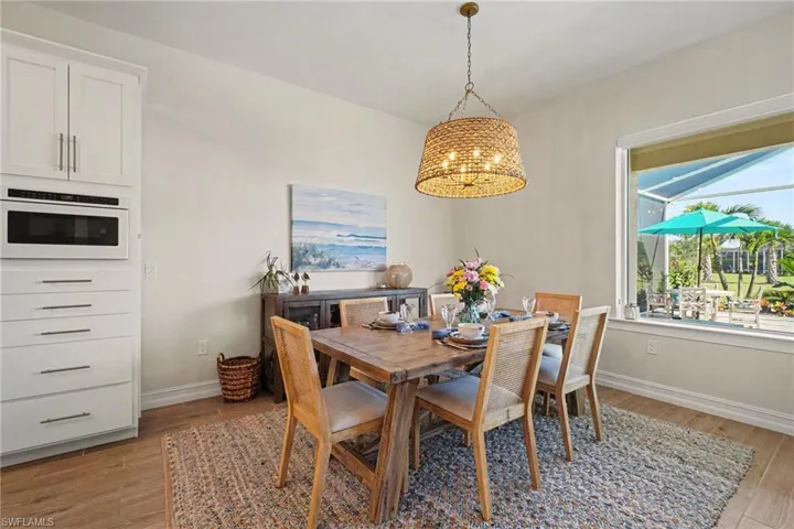Built-in white cabinetry with a microwave, wood-finish flooring, a woven pendant light fixture, and a large window overlooking a screened lanai