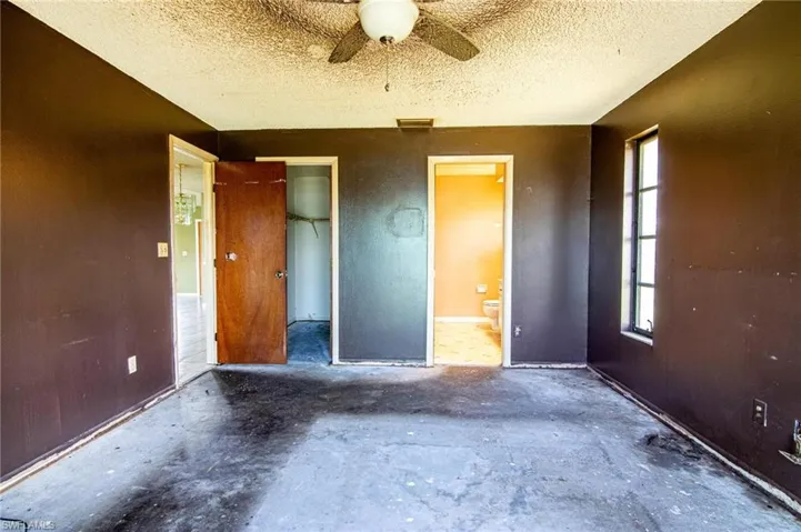 Unfurnished bedroom with a closet, connected bathroom, a textured ceiling, concrete flooring, and ceiling fan