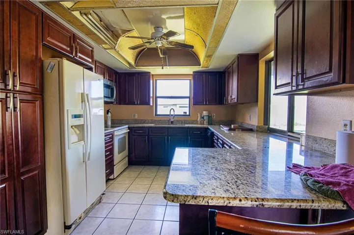 Kitchen featuring kitchen peninsula, white appliances, a wealth of natural light, and a raised ceiling
