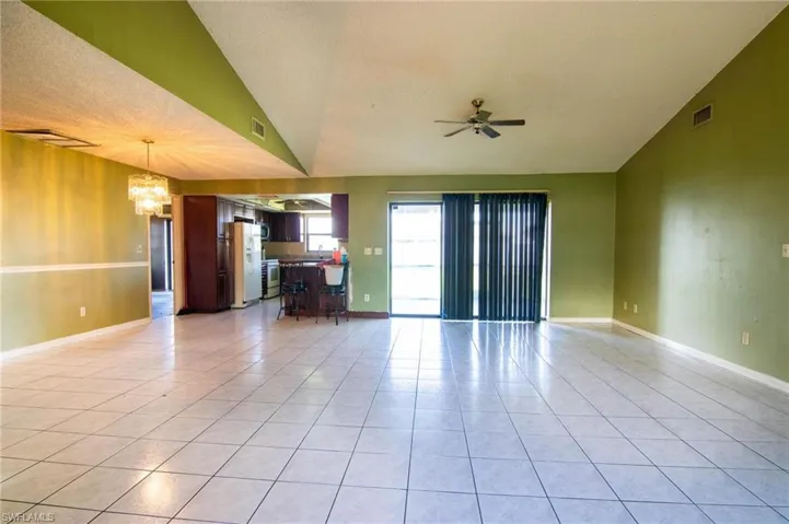 Unfurnished living room featuring a textured ceiling, ceiling fan with notable chandelier, light tile patterned floors, and vaulted ceiling