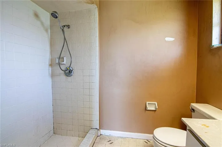 Bathroom with tiled shower, tile patterned floors, toilet, and vanity