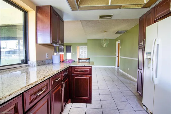 Kitchen with kitchen peninsula, hanging light fixtures, light tile patterned floors, a chandelier, and white fridge with ice dispenser