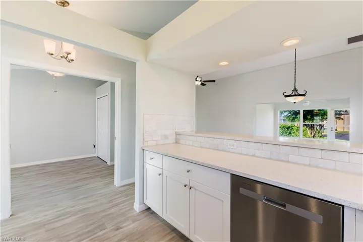 Kitchen with decorative light fixtures, white granite counters, dishwasher, white cabinetry, and decorative backsplash