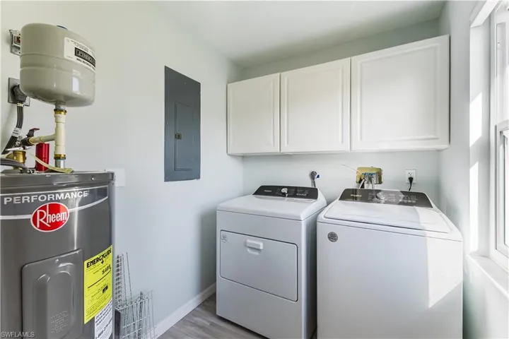 Laundry room featuring new electric water heater, cabinet space, washing machine and dryer, electric panel, and light wood finished floors