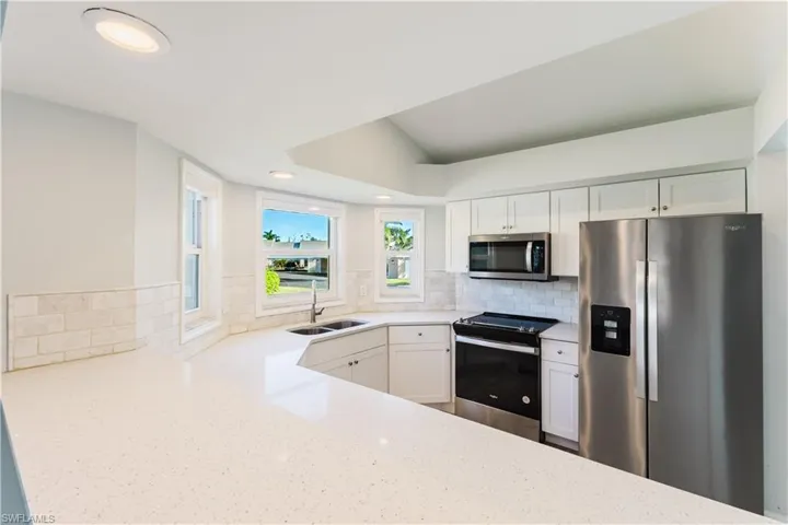 Kitchen with appliances with stainless steel finishes, white cabinets, recessed lighting, light stone counters, and backsplash