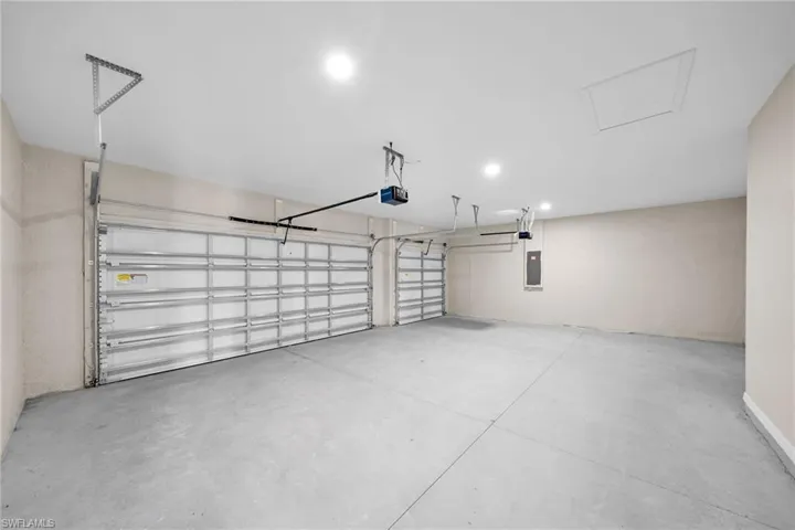 Garage with electric panel, recessed lighting, and a garage door opener