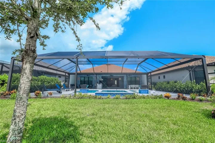 Back of house featuring glass enclosure, a pool with connected hot tub, a yard, and a patio