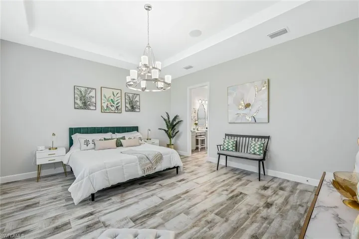 Bedroom featuring a chandelier, a raised ceiling, wood finished floors, and ensuite bath