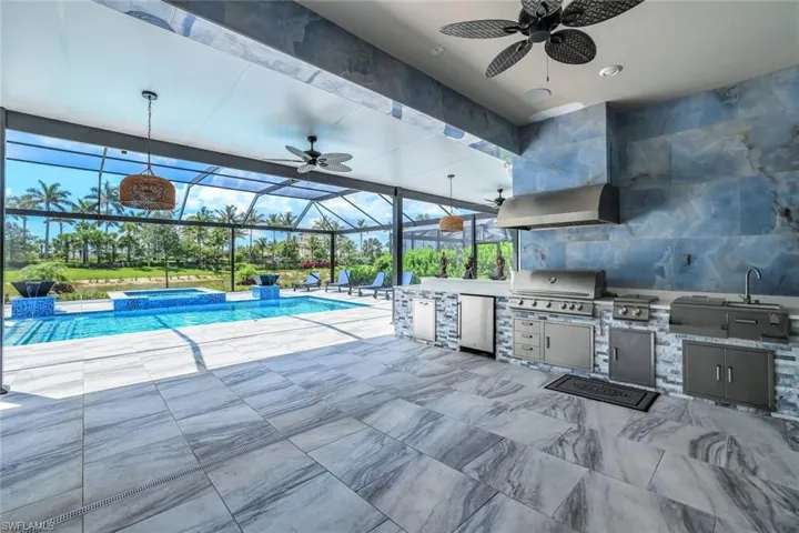 View of pool featuring an outdoor kitchen, a ceiling fan, a pool with connected hot tub, glass enclosure, and a patio