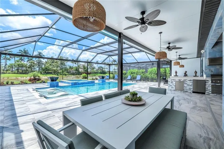 View of patio / terrace with an outdoor kitchen, ceiling fan, a pool with connected hot tub, a lanai, and outdoor dining space