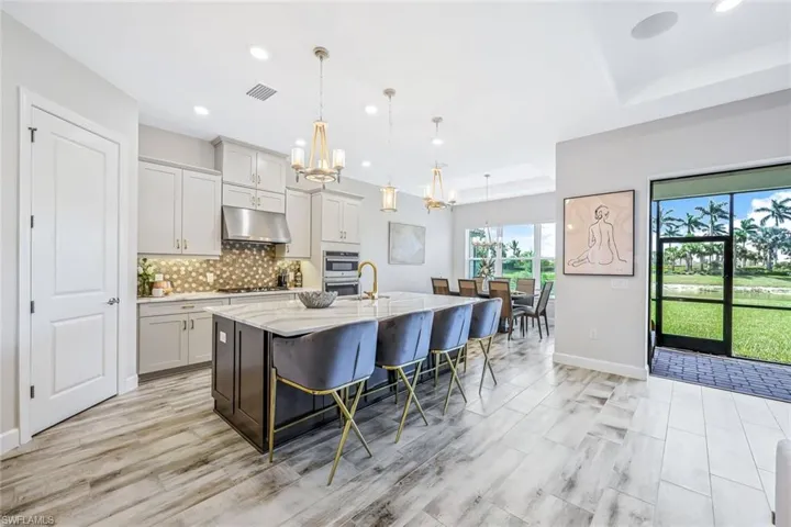 Kitchen featuring under cabinet range hood, a chandelier, a kitchen island with sink, light stone counters, and gas stovetop