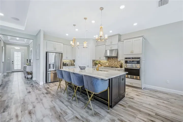 Kitchen with stainless steel appliances, a chandelier, under cabinet range hood, tasteful backsplash, and a large island with sink