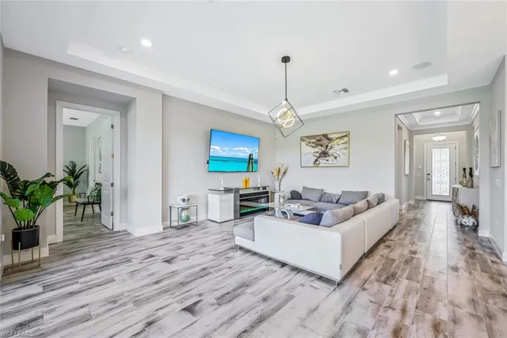 Living area with a raised ceiling, light wood-style flooring, recessed lighting, and plenty of natural light