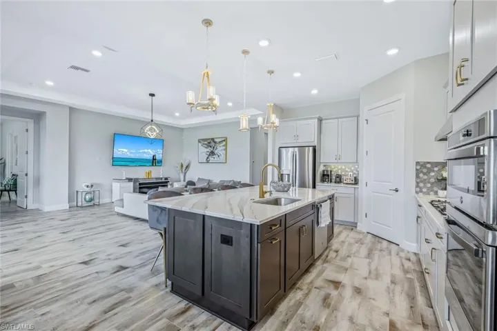 Kitchen with stainless steel appliances, a chandelier, tasteful backsplash, light wood-type flooring, and recessed lighting