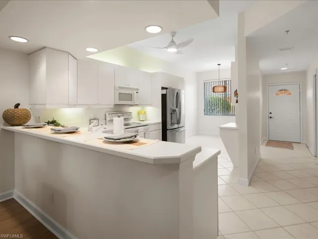 Kitchen with a peninsula, light countertops, hanging light fixtures, white appliances, and ceiling fan