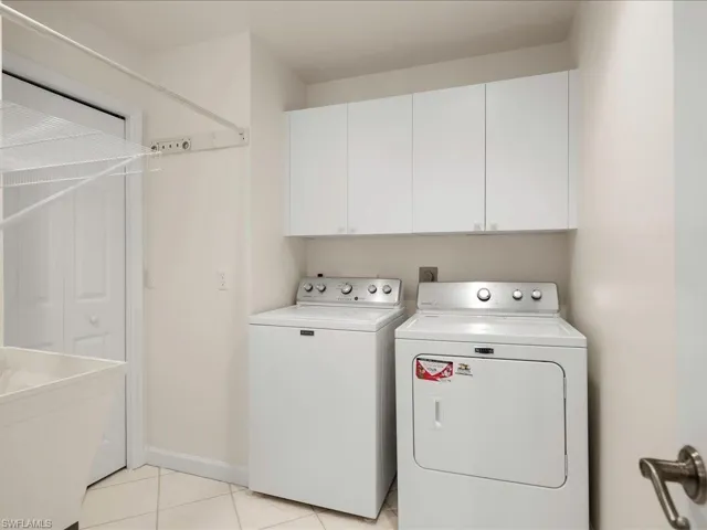 Washroom with independent washer and dryer, light tile patterned flooring, and cabinet space