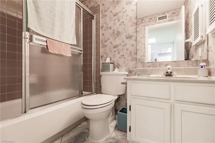 Full bathroom with shower / bath combination with glass door, vanity, wallpapered walls, and light tile patterned floors