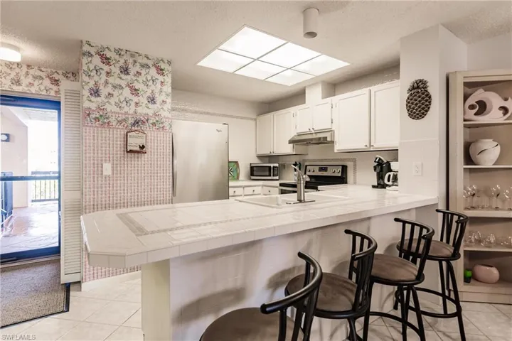 Kitchen featuring light tile patterned floors, a kitchen breakfast bar, stainless steel appliances, tile countertops, and a textured ceiling