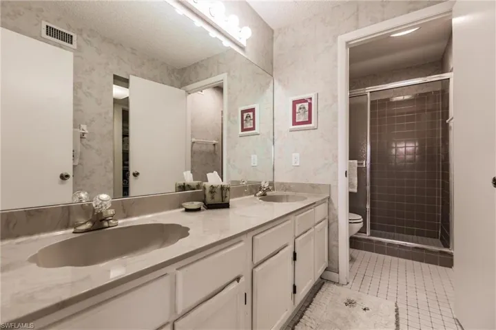 Full bathroom with a stall shower, double vanity, light tile patterned flooring, a textured ceiling, and wallpapered walls