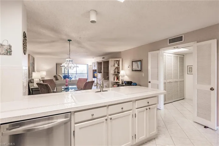 Kitchen with dishwasher, a textured ceiling, white cabinetry, light tile patterned floors, and open floor plan