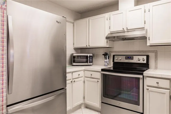 Kitchen with appliances with stainless steel finishes, white cabinetry, tile counters, under cabinet range hood, and tasteful backsplash
