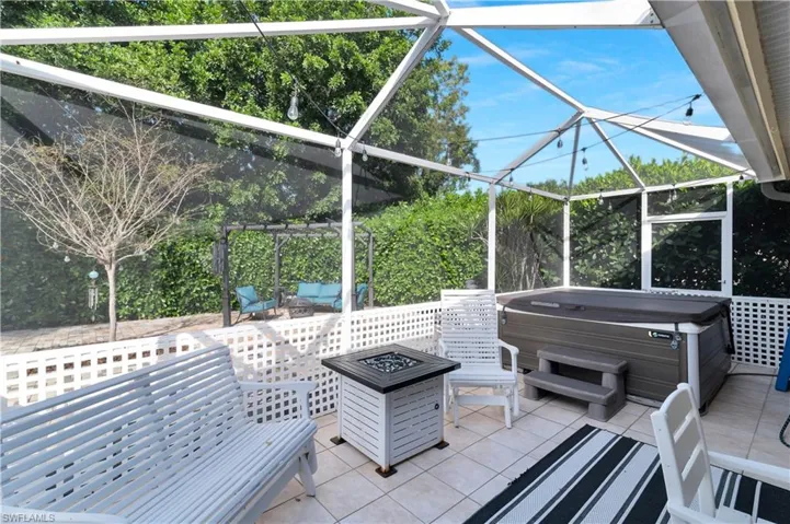 View of patio with a sunroom, glass enclosure, a hot tub, and view of scattered trees