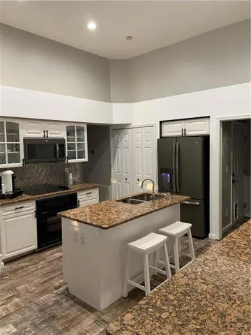 Kitchen with a high ceiling, refrigerator, wall oven, a kitchen island with sink, and tasteful backsplash