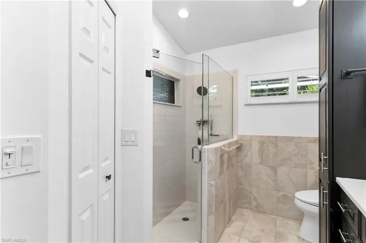 Bathroom with a closet, vanity, a shower stall, tile walls, and lofted ceiling