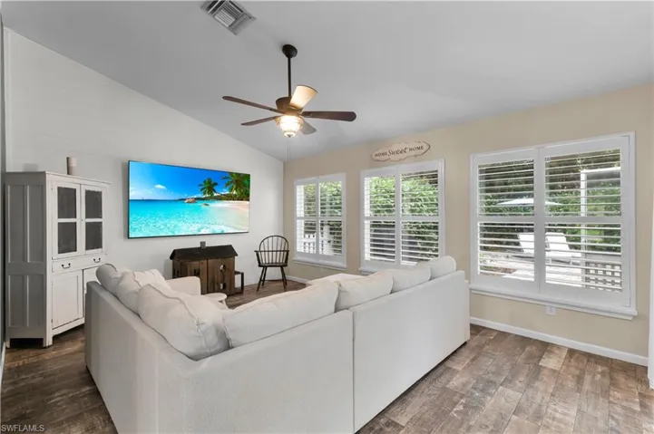 Living room featuring vaulted ceiling, dark wood-style floors, and ceiling fan