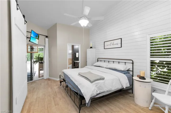 Bedroom featuring light wood finished floors, ensuite bathroom, wooden walls, and a ceiling fan