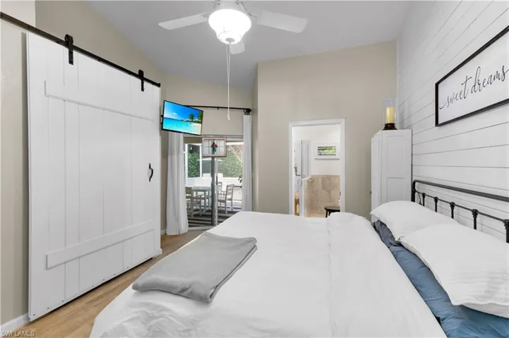 Bedroom featuring a barn door, a ceiling fan, light wood finished floors, access to exterior, and wood walls