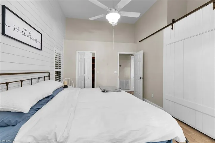 Bedroom featuring a barn door, wood finished floors, ceiling fan, a towering ceiling, and wood walls