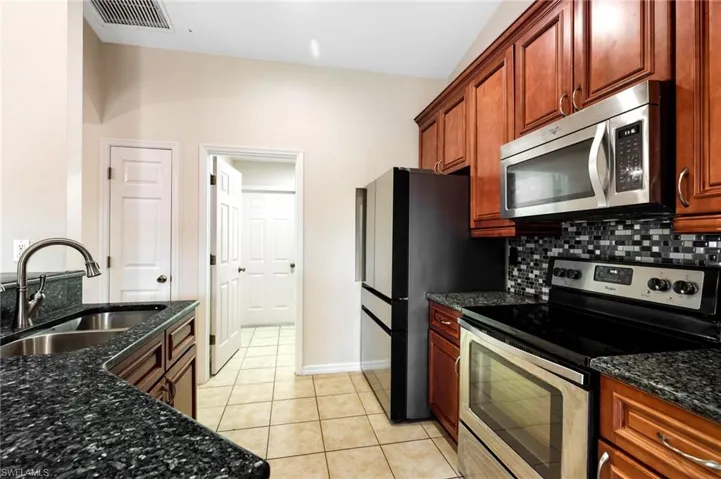 Kitchen with appliances with stainless steel finishes, tasteful backsplash, dark stone counters, sink, and light tile patterned floors
