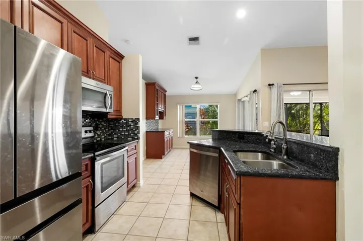 Kitchen with dark stone counters, sink, stainless steel appliances, and plenty of natural light