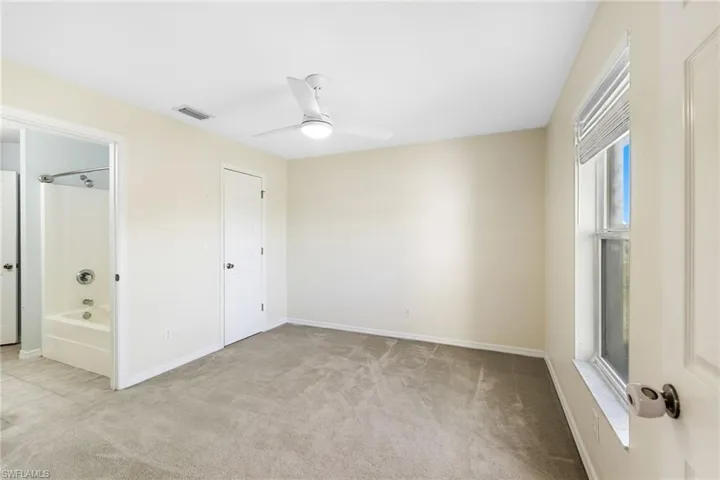 Unfurnished bedroom with connected bathroom, ceiling fan, a closet, and light colored carpet