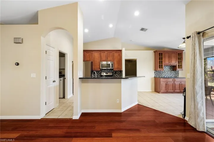 Kitchen featuring vaulted ceiling, light hardwood / wood-style flooring, tasteful backsplash, kitchen peninsula, and stainless steel appliances