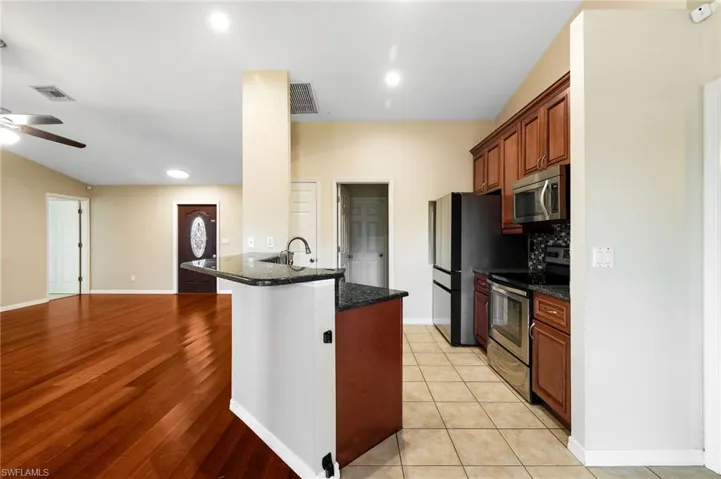 Kitchen with appliances with stainless steel finishes, light hardwood / wood-style flooring, ceiling fan, and dark stone counters