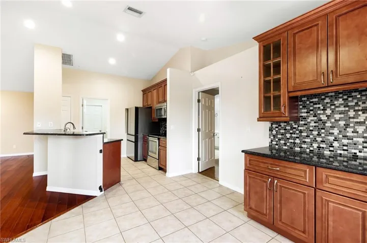 Kitchen with lofted ceiling, light hardwood / wood-style flooring, decorative backsplash, dark stone countertops, and stainless steel appliances