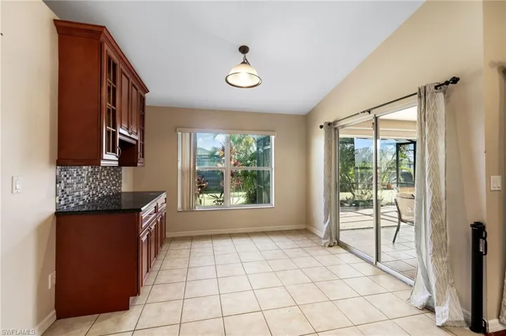 Kitchen with decorative backsplash, light tile patterned floors, vaulted ceiling, and dark stone countertops