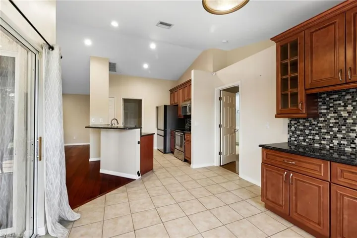 Kitchen with light hardwood / wood-style flooring, backsplash, dark stone counters, lofted ceiling, and appliances with stainless steel finishes