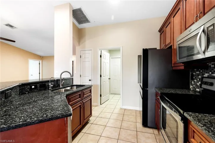 Kitchen with sink, dark stone countertops, vaulted ceiling, light tile patterned flooring, and appliances with stainless steel finishes