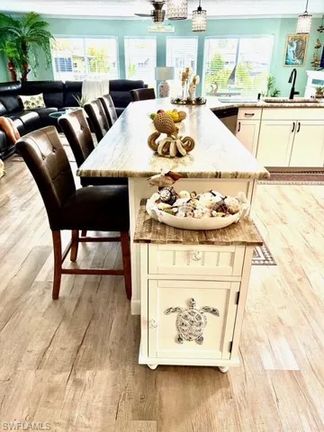 Kitchen featuring white cabinets, light wood-style floors, ornamental molding, open floor plan, and light stone counters