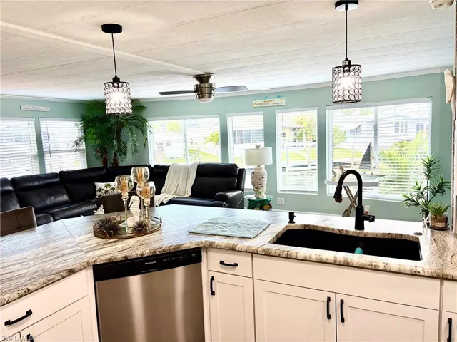 Kitchen featuring stainless steel dishwasher, open floor plan, white cabinetry, ceiling fan, and light stone countertops
