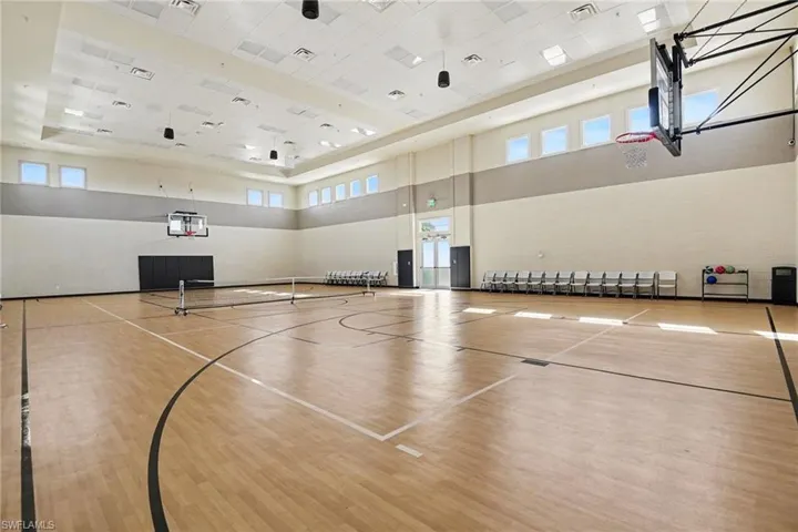 Indoor athletic court with light wood-finish flooring, high ceilings, and multiple windows providing natural light