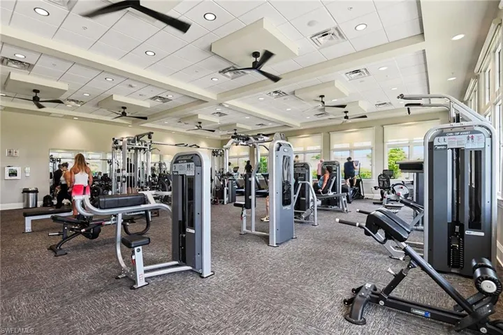 Spacious fitness center featuring various exercise equipment, carpet flooring, multiple ceiling fans, recessed lighting, and large windows with blinds